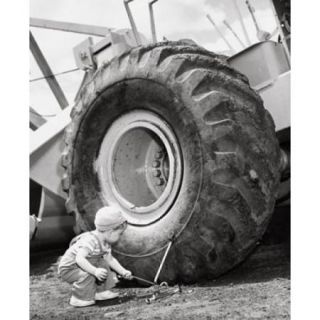 Boy holding a tool and crouching near a bulldozer Poster Print (18 x 24)